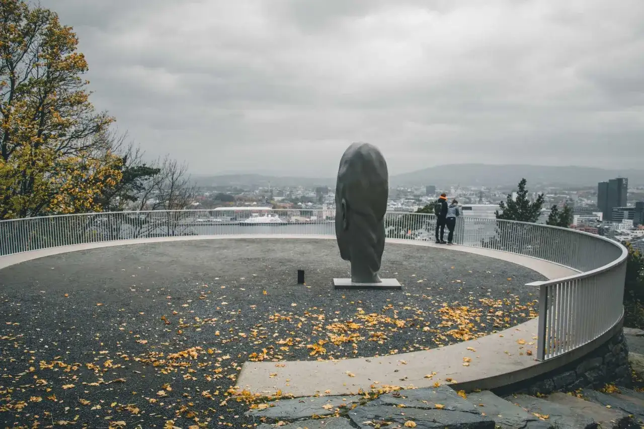 Punkt widokowy Oslo z rzeźbą głowy i parą podziwiającą panoramę miasta. Jesienne liście na ziemi.