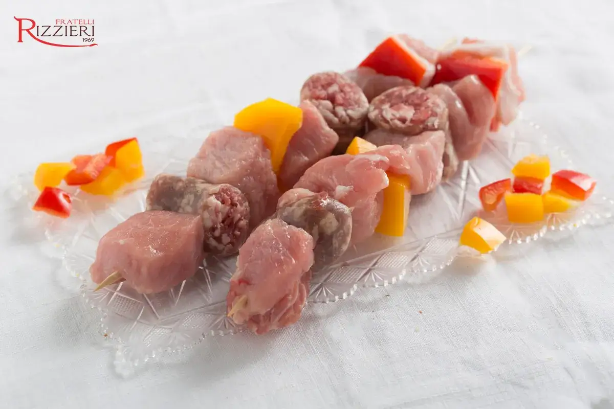 Spiedini di carne mista con peperoni rossi e gialli, pronti per la griglia.