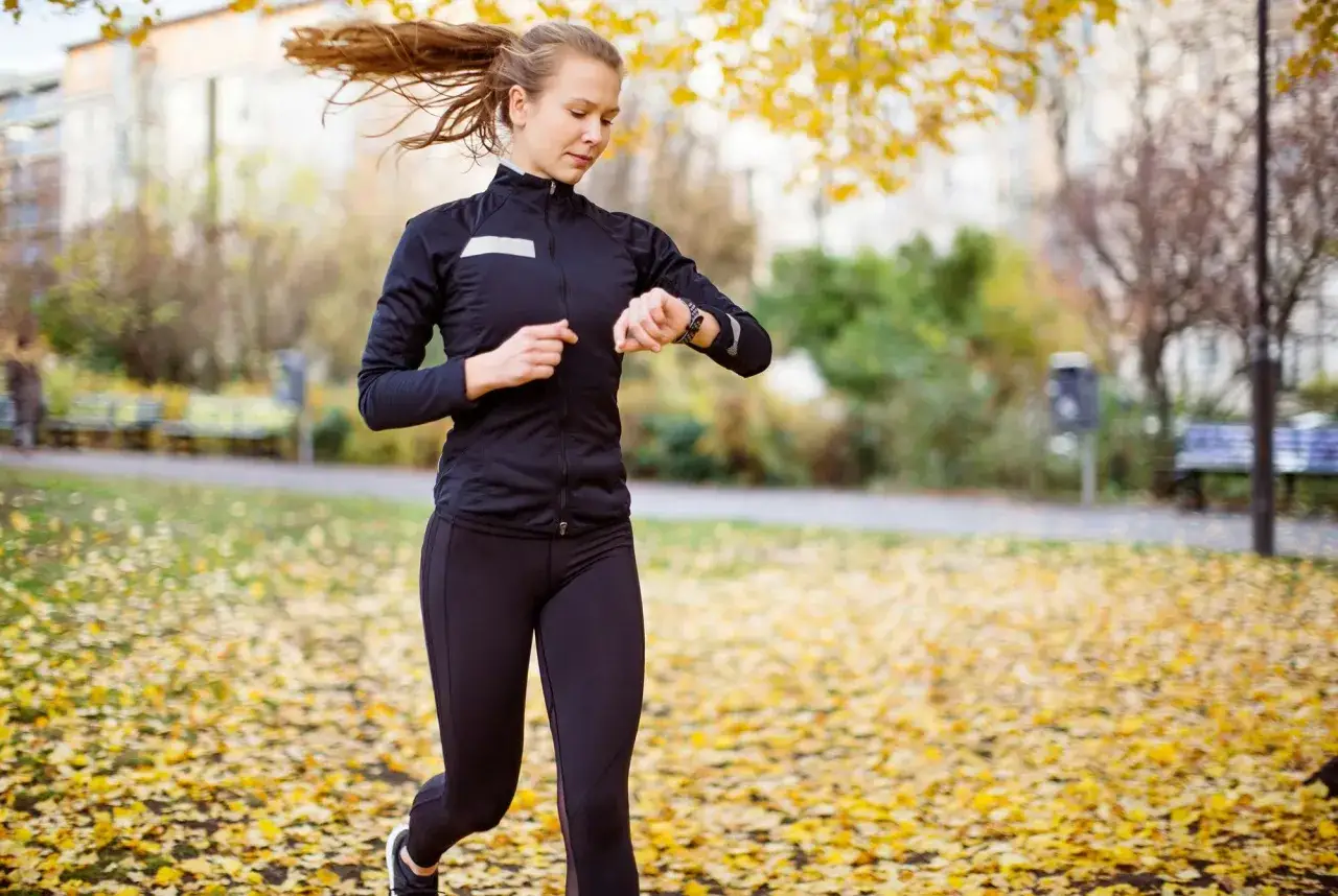 En kvinna springer i en park täckt av höstlöv och kollar sin klocka, hon verkar ha en bra tid på 5 km.