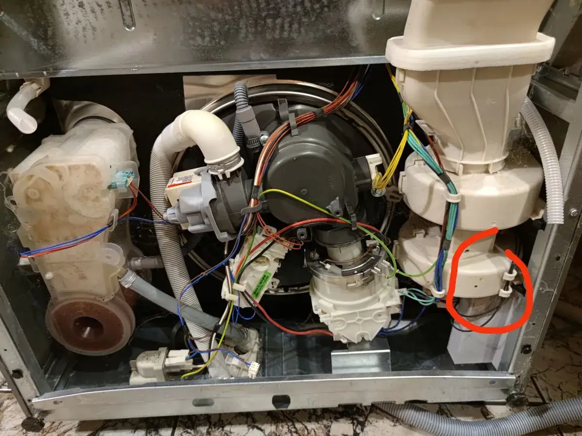 Wnętrze zmywarki Whirlpool z widocznym błędem E4. Czerwone kółko zaznacza potencjalny problem z pompą.