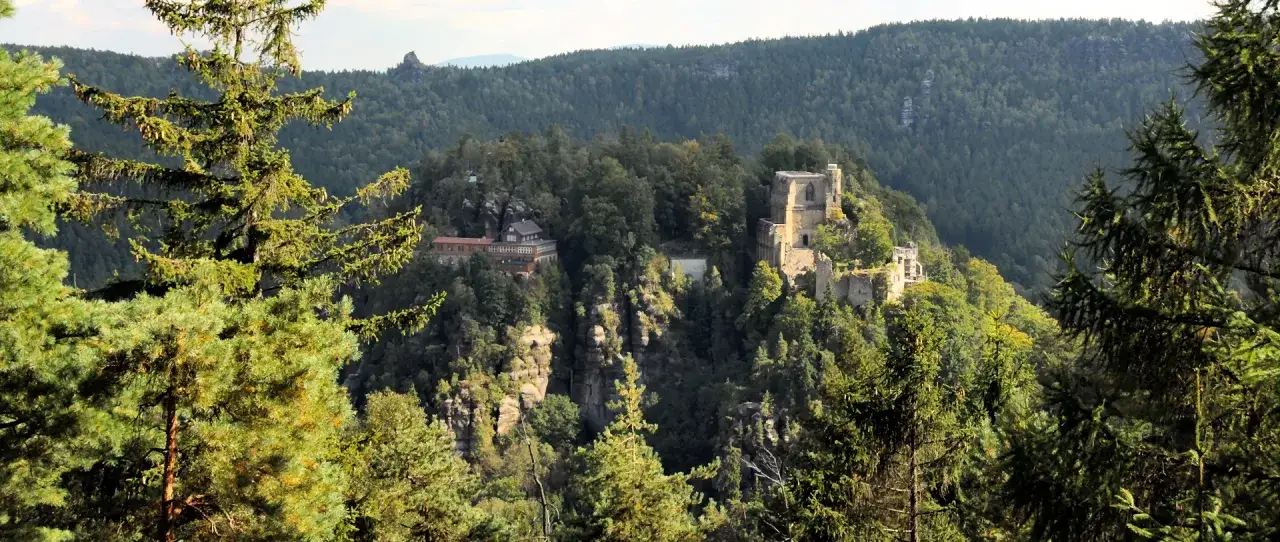 Blick auf die Ruine Burg Oybin und ein Gasthaus im Zittauer Gebirge, umgeben von dichten W&auml;ldern und Felsen.