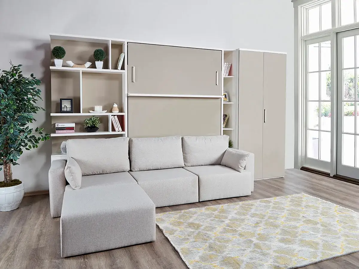 Ein gem&uuml;tliches Wohnzimmer mit Sofa und einem cleveren versteckten Bett im Schrank. B&uuml;cherregale und eine Pflanze schm&uuml;cken den Raum.