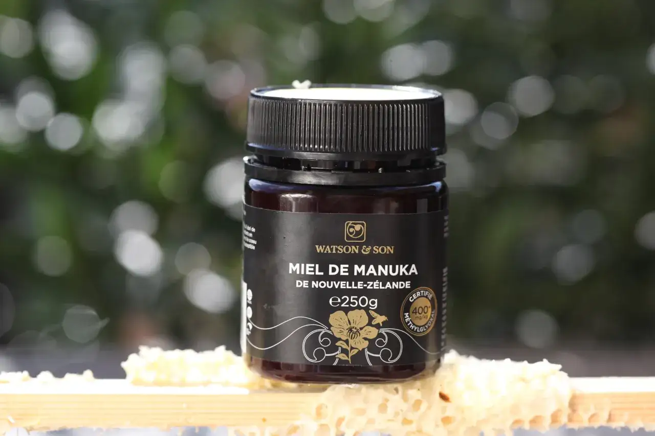 Un pot de miel de Manuka Watson & Son, certifié 400 mg/kg de méthylglyoxal, posé sur des rayons de miel. Découvrez les miel de manuka bienfaits.