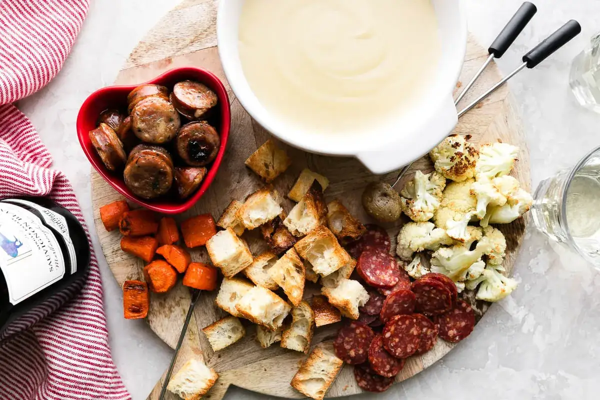 Köstliches Fondue mit vielfältigen Beilagen: Brot, Wurst, Karotten, Blumenkohl und Salami. Ein bunter Salat fehlt hier nicht, um das Genusserlebnis abzurunden.
