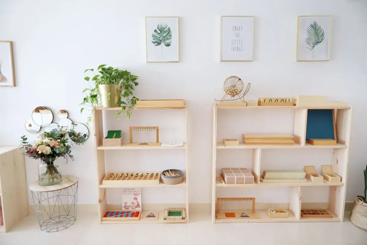 Un rincón Montessori con estanterías de madera llenas de materiales educativos, plantas y arte en las paredes.