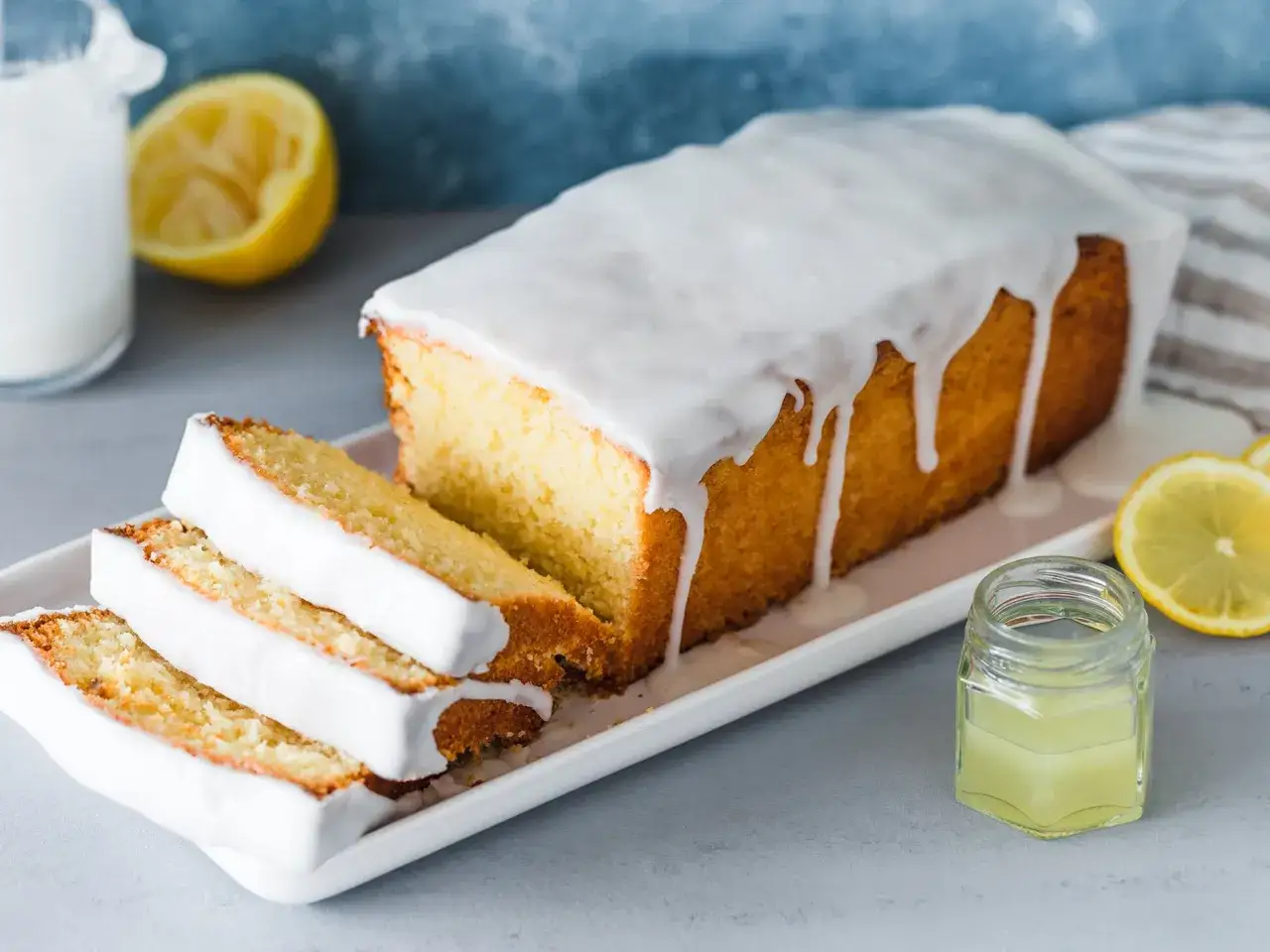 Saftiger zitronenkuchen in Kastenform, mit s&uuml;&szlig;em Zuckerguss &uuml;berzogen und in Scheiben geschnitten. Ein Hauch von Zitrone und Milch runden das Bild ab.
