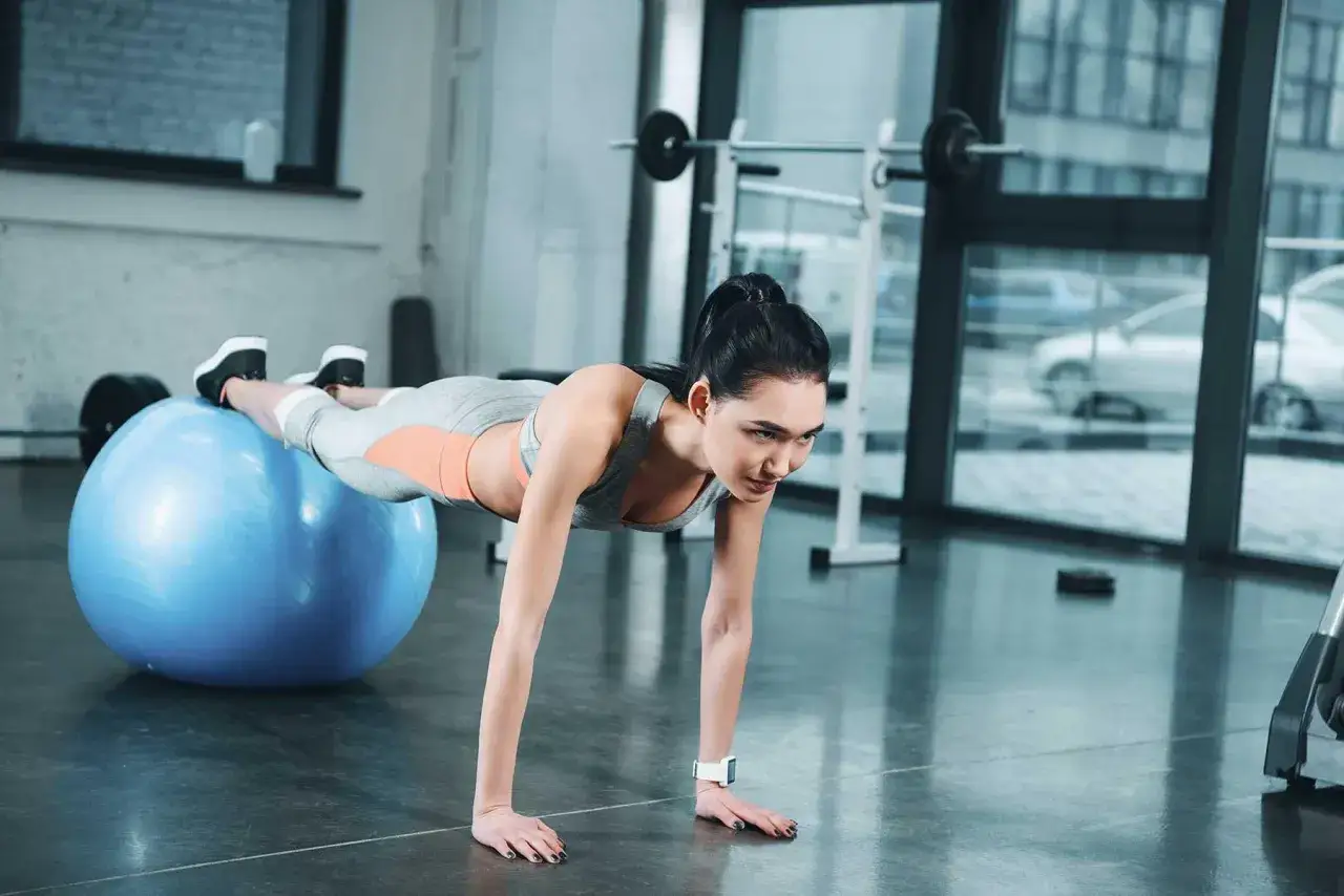 Donna esegue addominali con la palla, mantenendo la posizione plank con i piedi appoggiati sulla palla svizzera.