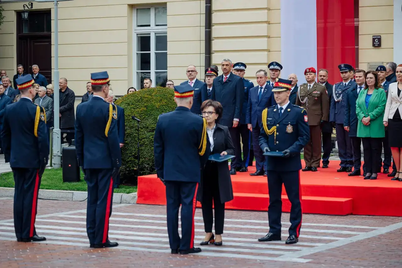 Uroczystość z udziałem straży marszałkowskiej. Mundurowi stoją na baczność przed budynkiem, obok flagi Polski.