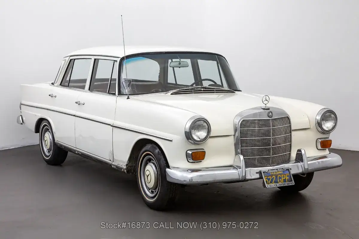 Biały Mercedes 200 z lat 60. z chromowanymi detalami i charakterystyczną atrapą chłodnicy.