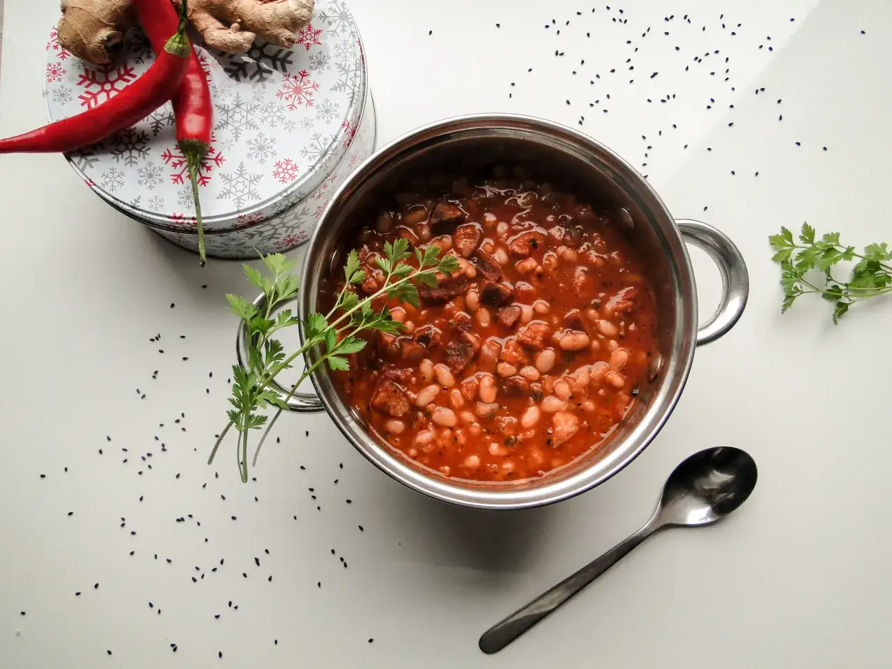 Gęsta, aromatyczna fasolka po bretońsku przepis babci w garnku, ozdobiona natką pietruszki. Obok leżą papryczki chili i imbir.