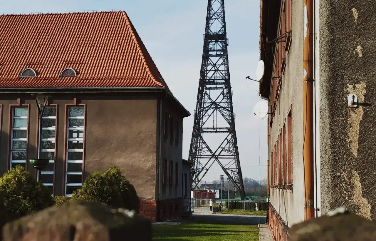 Wieża radiowa w Gliwicach, idealna na jednodniowe wycieczki z Gliwic. Obok budynki z czerwonym dachem i antenami satelitarnymi.
