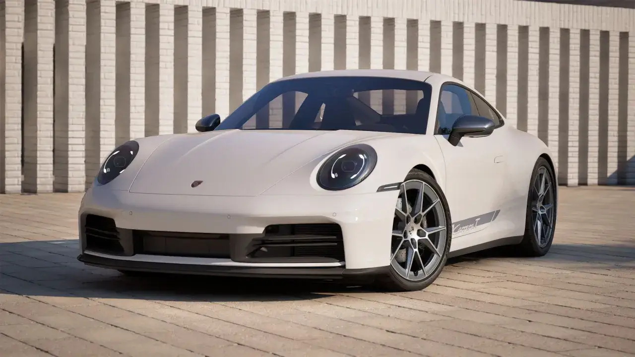 Białe Porsche 911 Carrera T z szarymi felgami i naklejką na progu, zaparkowane na kamiennym podjeździe przed nowoczesnym budynkiem.