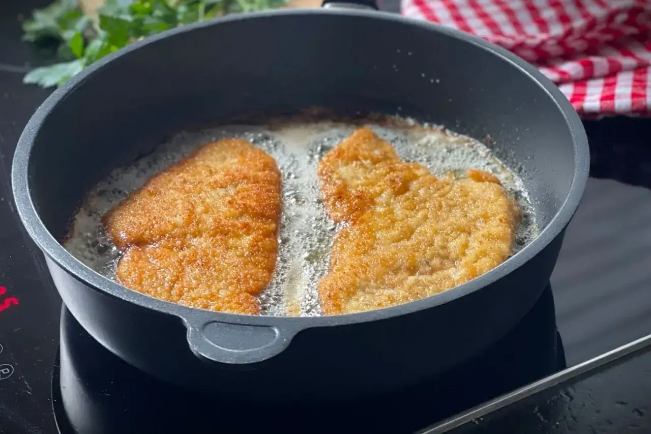 Zwei goldbraune Schnitzel brutzeln in hei&szlig;em &Ouml;l in einer Pfanne. Ein Cordon Bleu ist in Arbeit.