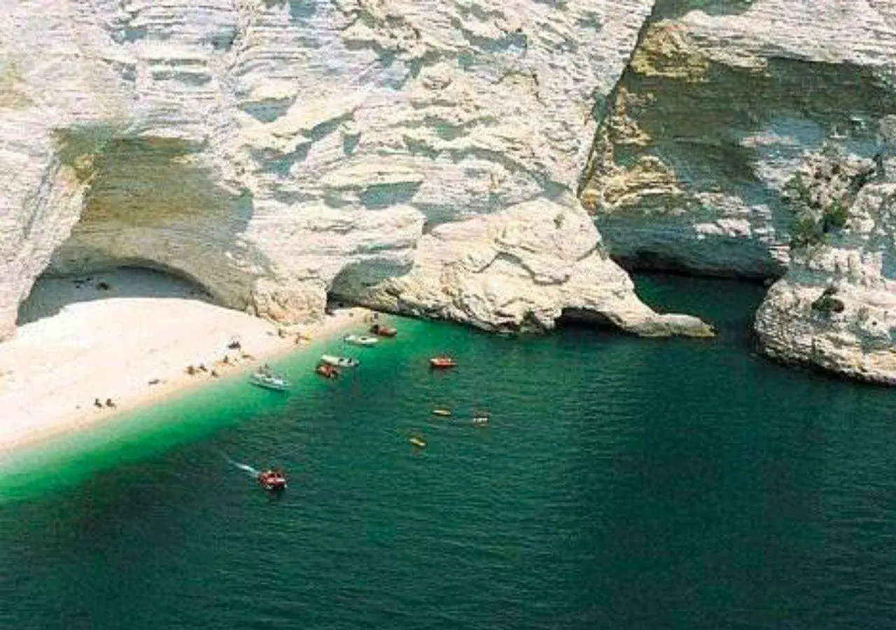 Spiaggia bianca incastonata tra alte falesie calcaree, con acque verdi e trasparenti. Barche e persone godono del sole e del mare a Manfredonia.