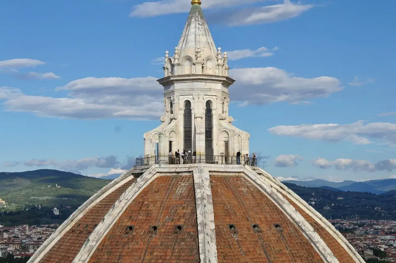 Widok na kopułę katedry Santa Maria del Fiore we Florencji. Ludzie podziwiają panoramę miasta z tarasu widokowego.