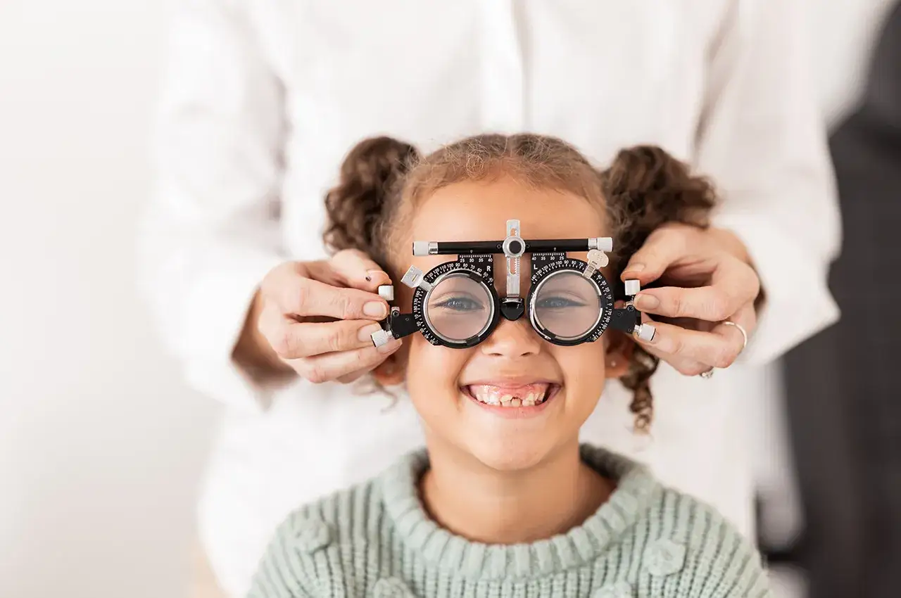 Mała dziewczynka uśmiecha się, gdy optometrysta zakłada jej okulary próbne. Czy nie noszenie okularów pogarsza wzrok? Sprawdźmy!