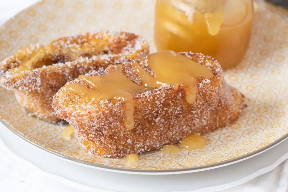 Torrijas de miel, doradas y rebozadas en azúcar, con un jarabe dorado cayendo.