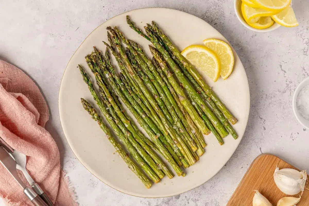 Espárragos trigueros crujientes hechos en airfryer, servidos en plato con rodajas de limón y sal.