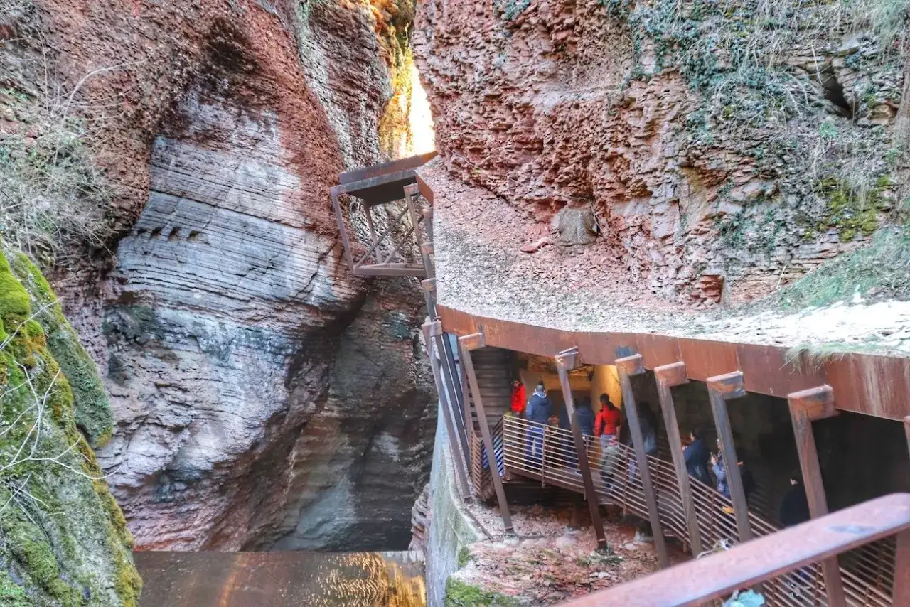 Un orrido ponte alto attraversa una gola rocciosa, con persone che percorrono una passerella metallica.