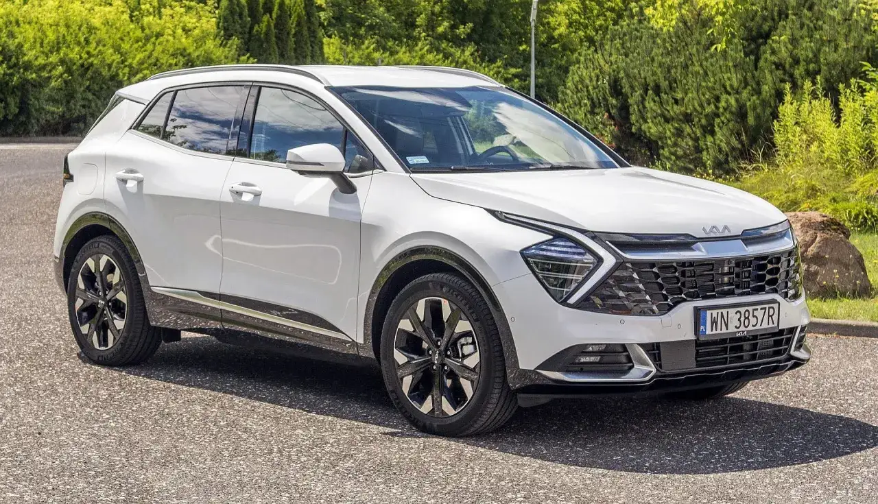 Biały Kia Sportage 1.6 benzyna zaparkowany na tle zieleni. Elegancki SUV z nowoczesnym designem.