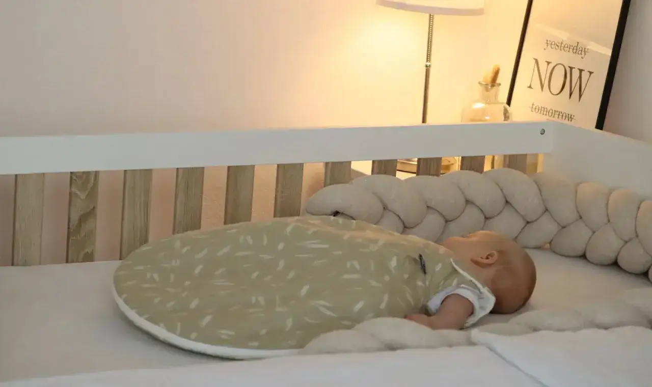Ein Baby schl&auml;ft friedlich in seinem Bettchen, eingeh&uuml;llt in einen gem&uuml;tlichen Schlafsack. Die weiche Bettumrandung bietet zus&auml;tzliche **baby begrenzung schlafen** und Geborgenheit.