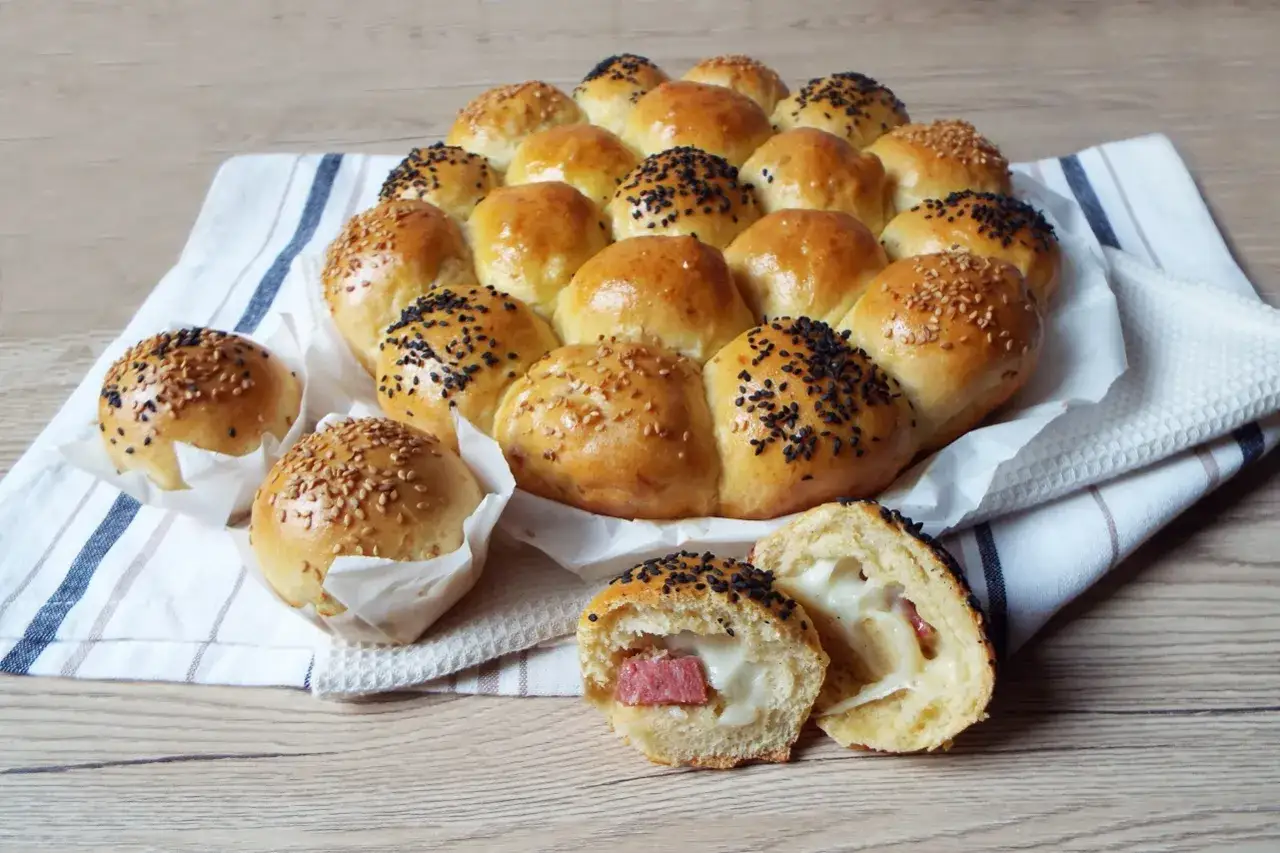 Pane soffice a forma di grappolo, alcuni con semi di sesamo, altri con semi neri. Uno aperto rivela un ripieno filante, un vero danubio salato.
