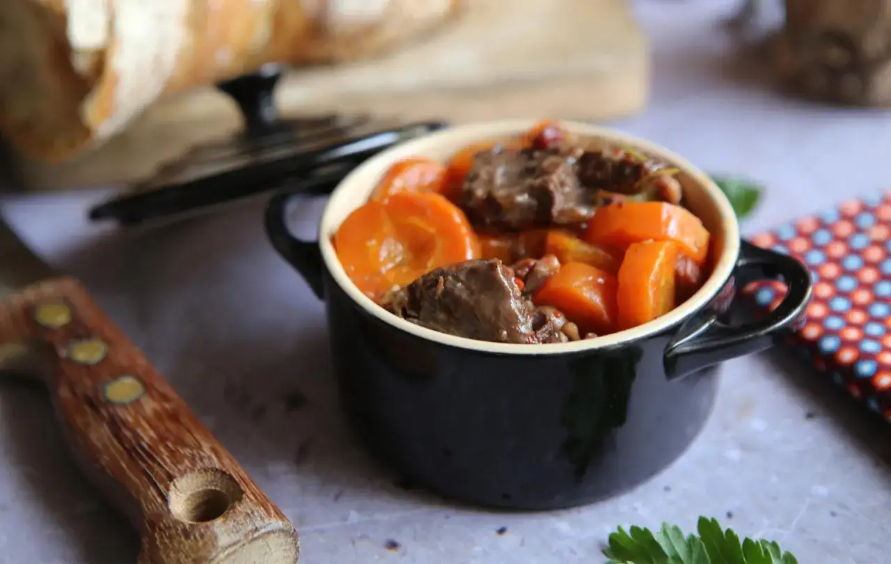 Un plat mijot&eacute; de joue de b&oelig;uf avec des carottes, pr&ecirc;t &agrave; &ecirc;tre d&eacute;gust&eacute;. Un couteau et du pain sont &agrave; proximit&eacute;.