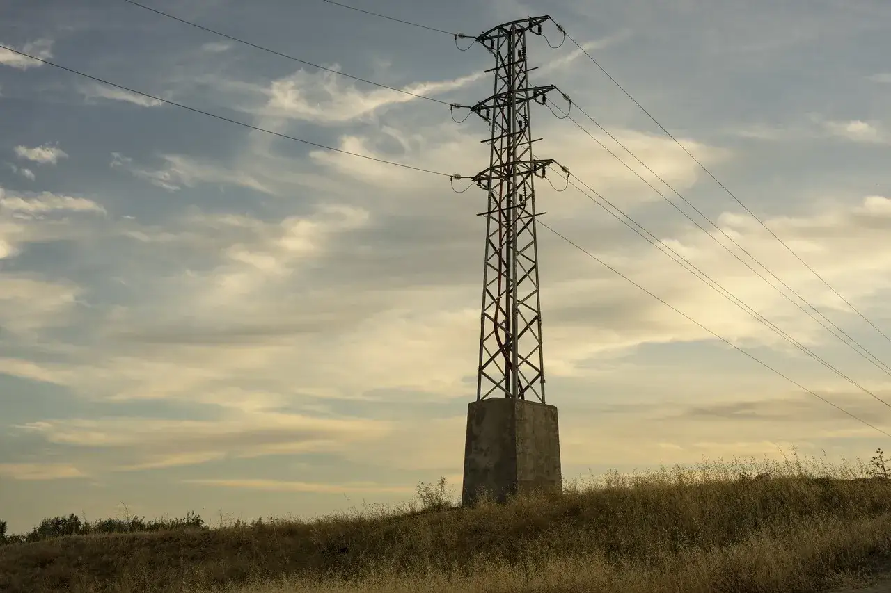 Wysoki słup energetyczny na tle nieba z chmurami, symbolizujący dystrybucję energii elektrycznej.
