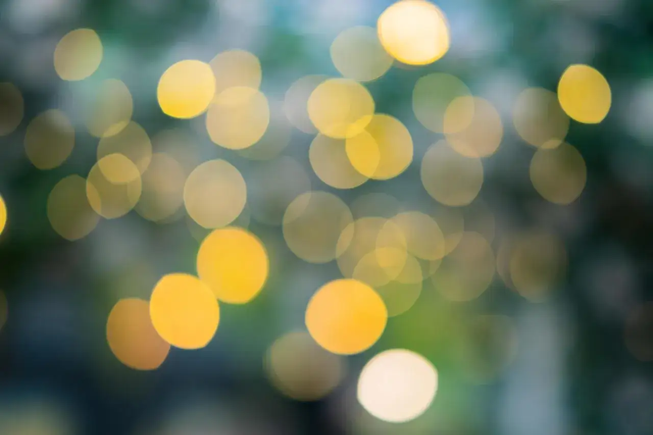 Rozmyte, złote kręgi światła tworzą magiczny bokeh na tle zieleni i błękitu.