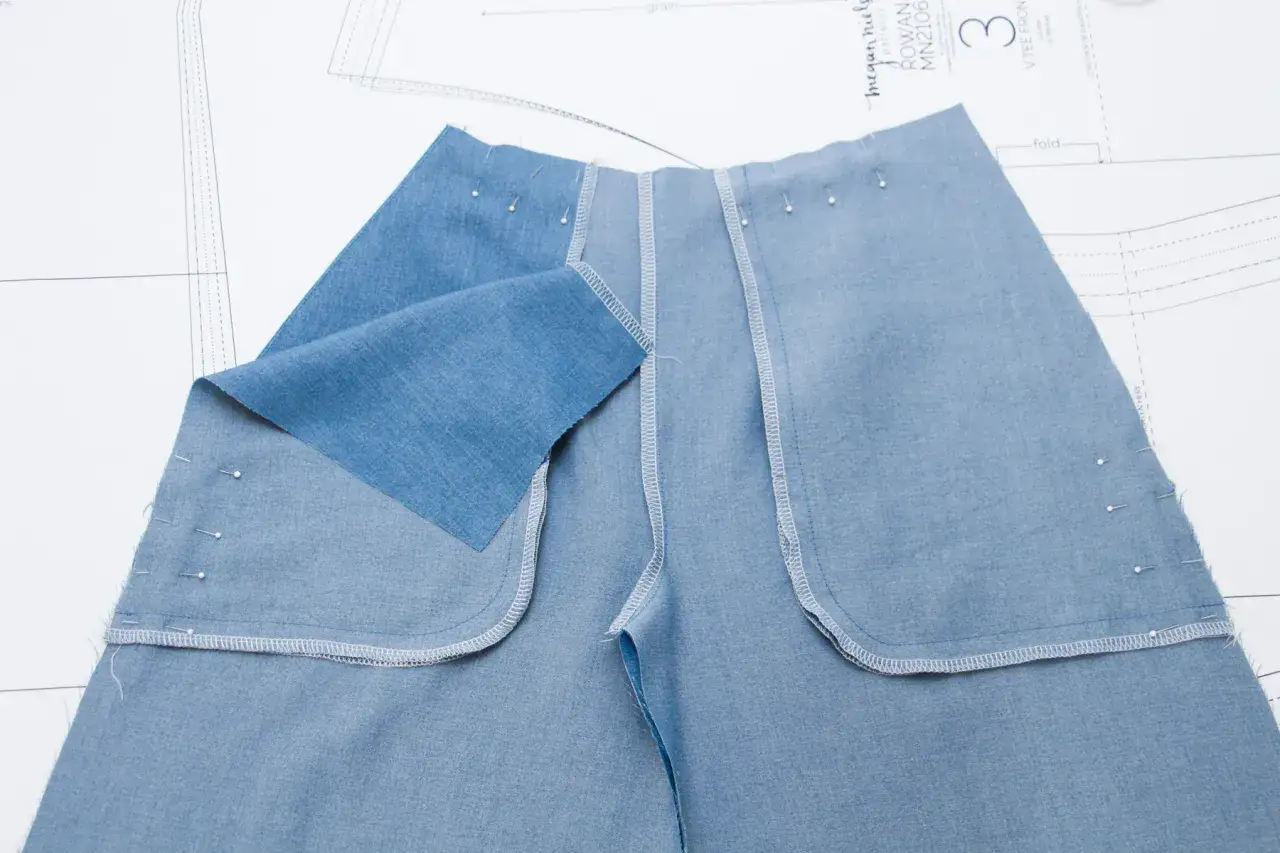 Pièces de tissu bleu denim épinglées sur un patron de couture, prêtes pour la création d'une poche italienne.