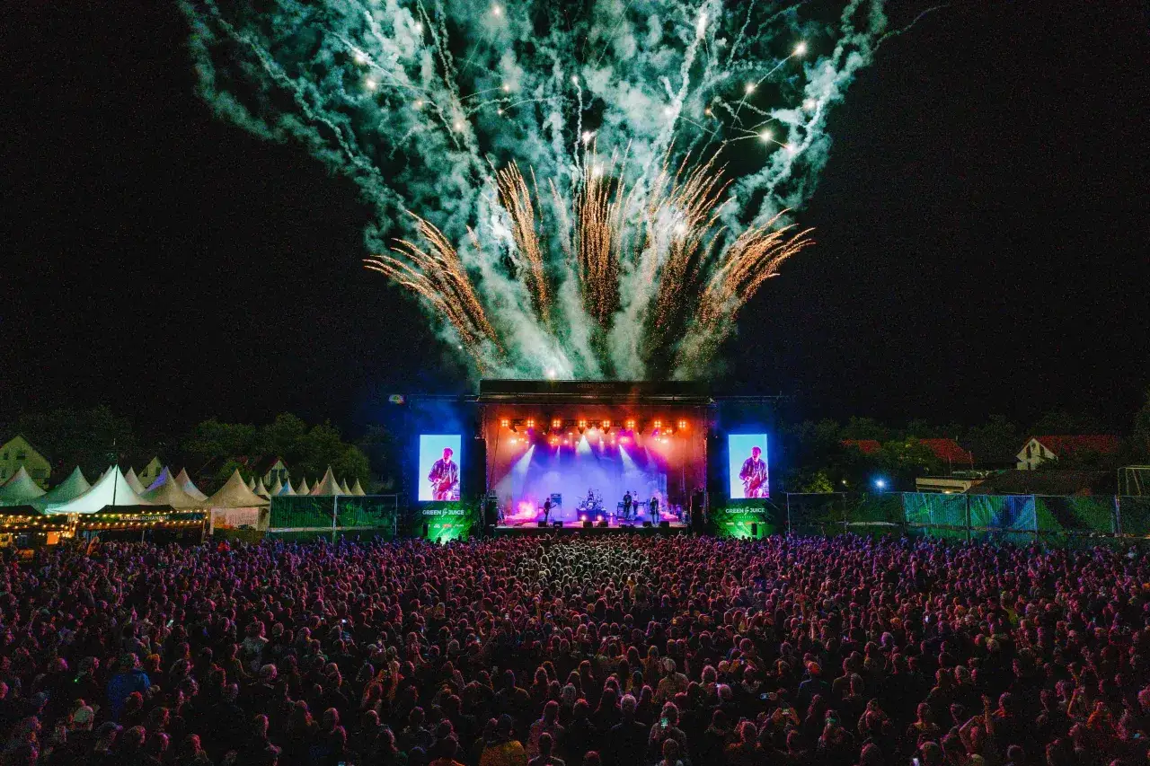 Feuerwerk &uuml;ber der B&uuml;hne beim Green Juice Festival. Tausende Fans jubeln einer Band zu, die auf der beleuchteten B&uuml;hne spielt.