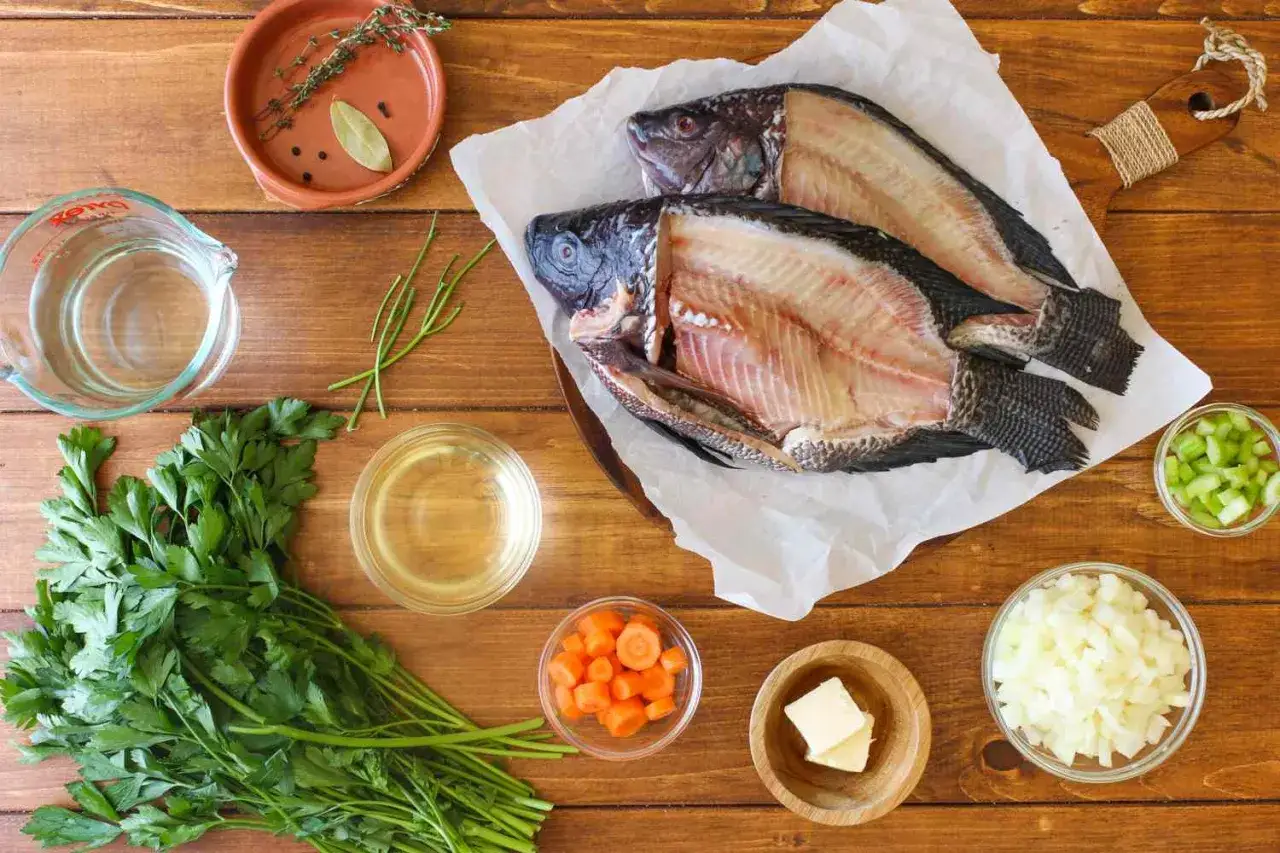 Deux poissons entiers pr&ecirc;ts &agrave; &ecirc;tre cuisin&eacute;s, accompagn&eacute;s de persil, carottes, oignons, c&eacute;leri, beurre, eau et &eacute;pices pour un d&eacute;licieux fumet de poisson.