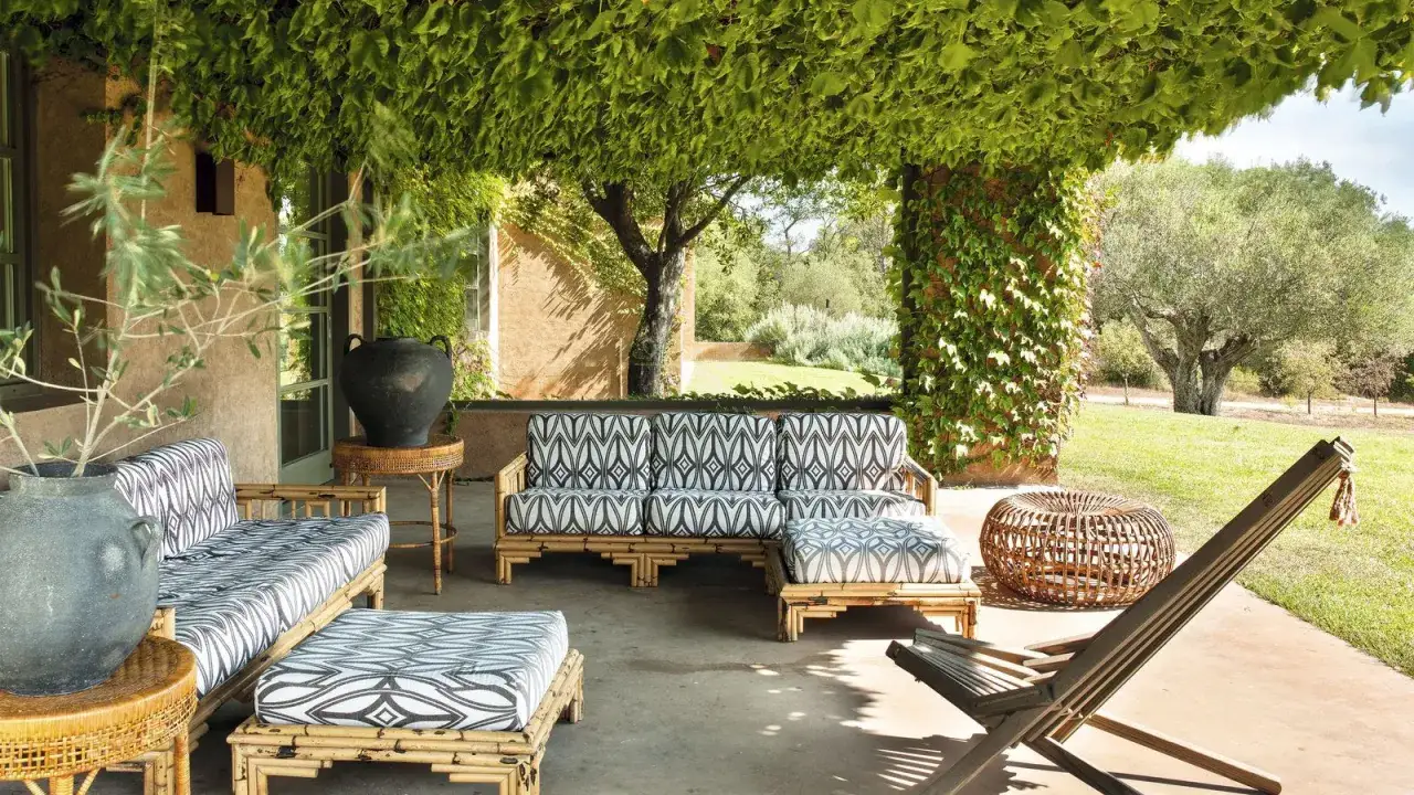 Terraza con muebles de bambú y cojines estampados, cubierta por exuberantes plantas trepadoras que no ensucian.