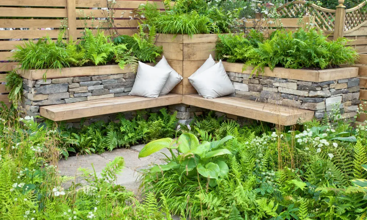 Ein gem&uuml;tlicher kleiner garten mit Steinmauern, Holzbank und vielen Farnen. Perfekt zum Entspannen.