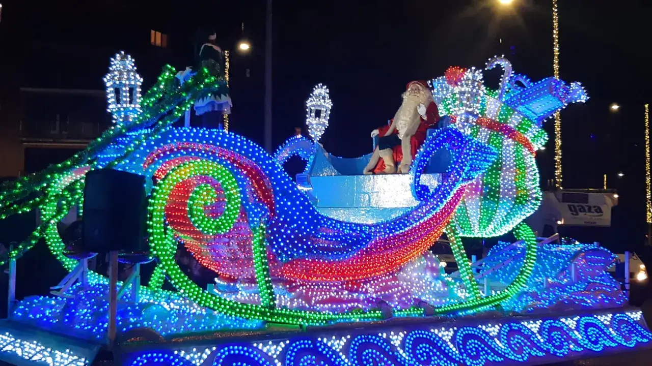 Papá Noel en su trineo iluminado, parte de una espectacular cabalgata navideña llena de luces de colores.