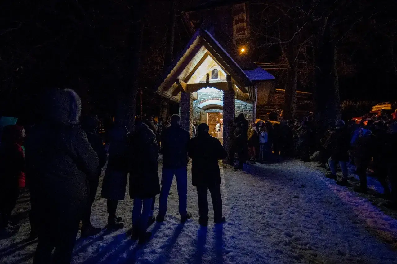 Nocna pasterka w Zakopanem. Ludzie zgromadzeni przed oświetloną kapliczką, śnieg na ziemi.