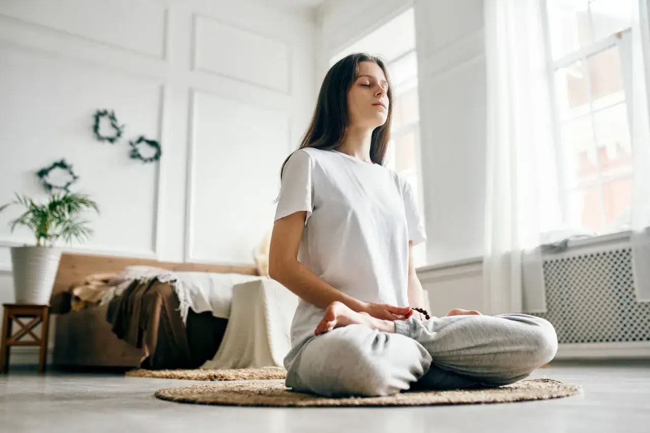 Ung kvinna i meditation position på en matta i ett ljust rum.