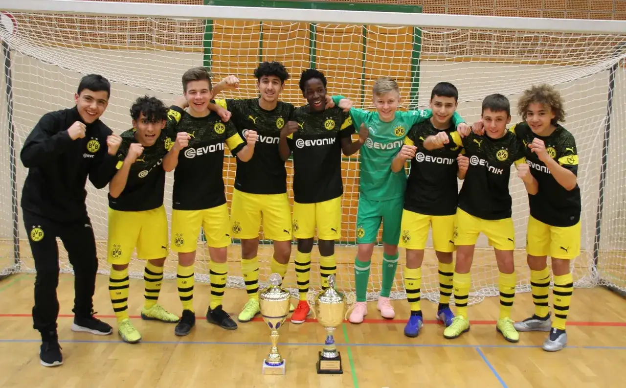 Junge Fußballer der BVB U14 jubeln mit Pokalen.