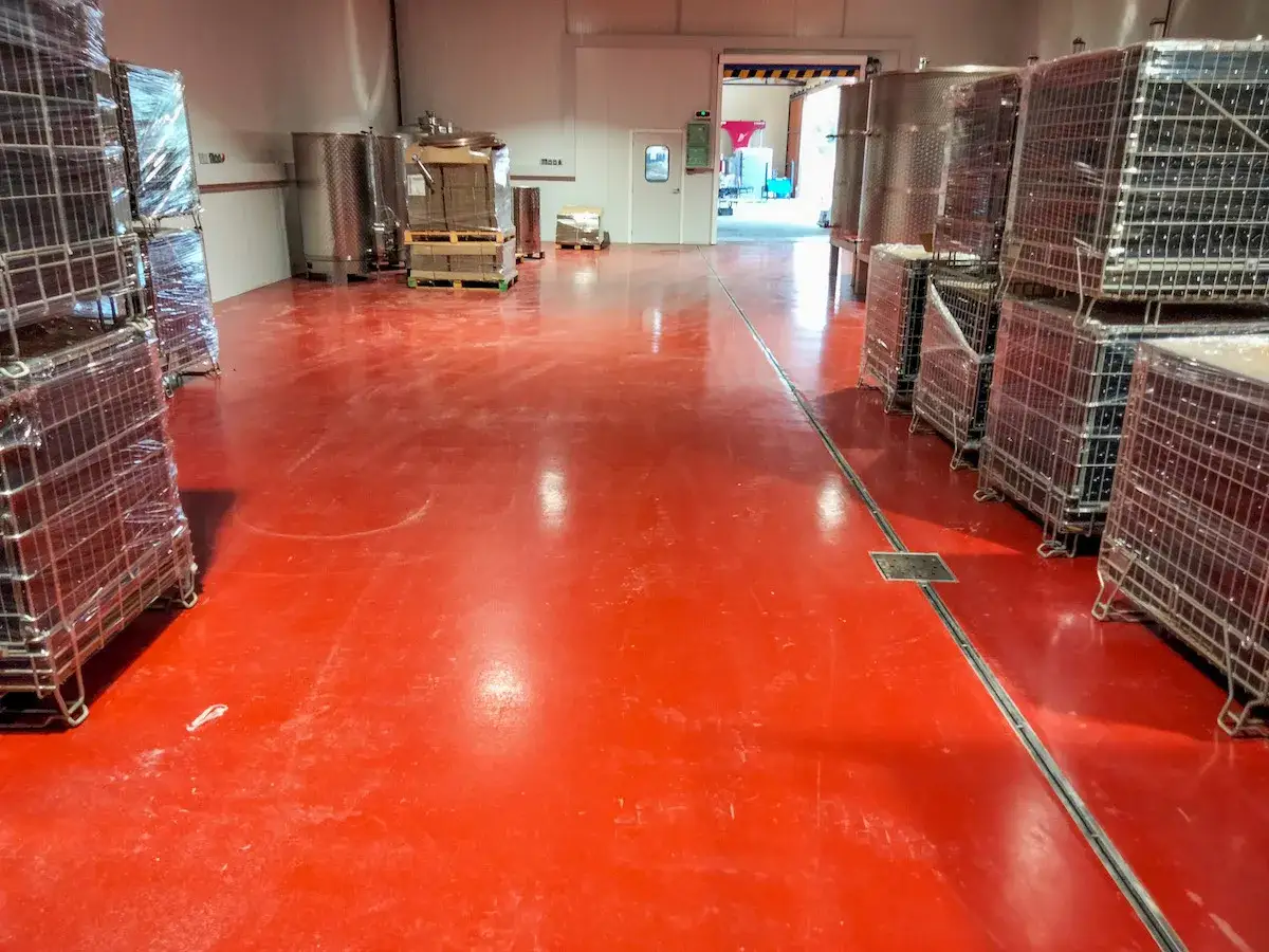 Suelos para bodegas de color rojo brillante, con estanter&iacute;as met&aacute;licas apiladas y tanques de acero inoxidable.