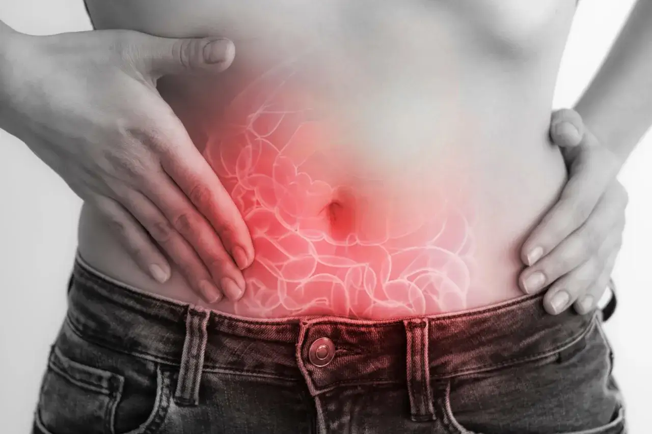 Manos sobre abdomen con inflamación intestinal, sugiriendo cómo expulsar los gases y aliviar el malestar.