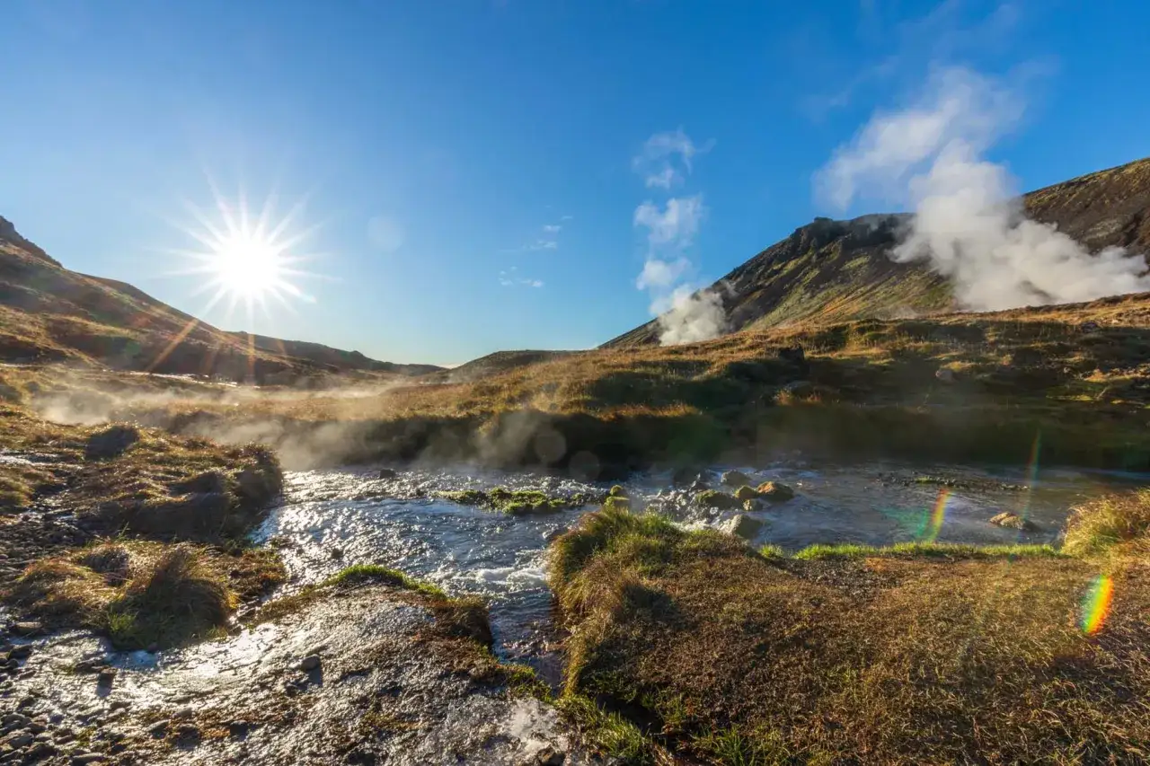 Słońce przebija się przez mgłę unoszącą się nad gorącą rzeką Islandia. Wulkaniczne krajobrazy i para tworzą magiczną atmosferę.