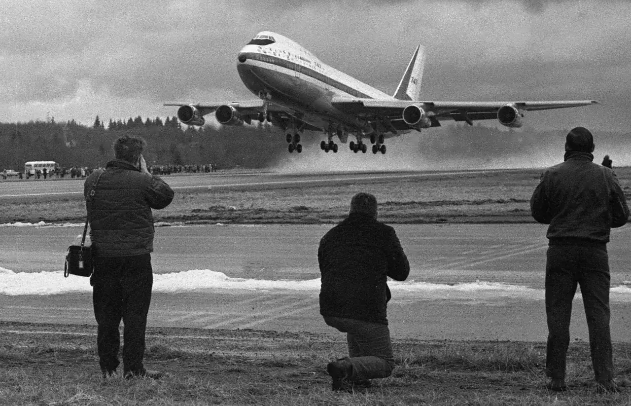 Pierwszy lot samolotem, odczucia ekscytacji i podziwu. Trzech mężczyzn obserwuje start Boeinga 747, jeden klęczy, dwóch stoi z aparatami.