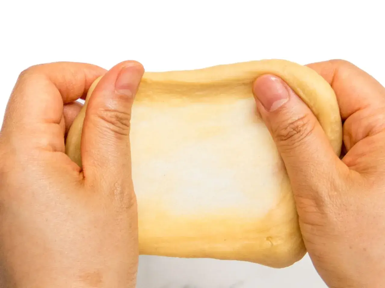 Hände dehnen einen glatten, homogenen Teig. Die Textur ist weich und elastisch, bereit für die Weiterverarbeitung.