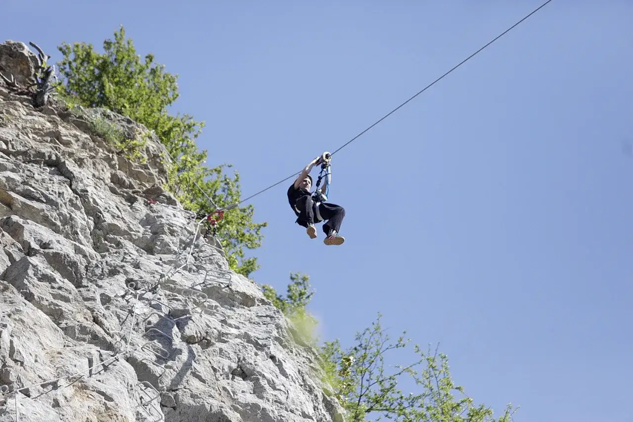Osoba zjeżdża na linie nad skalną ścianą z ubezpieczeniami via ferrata.