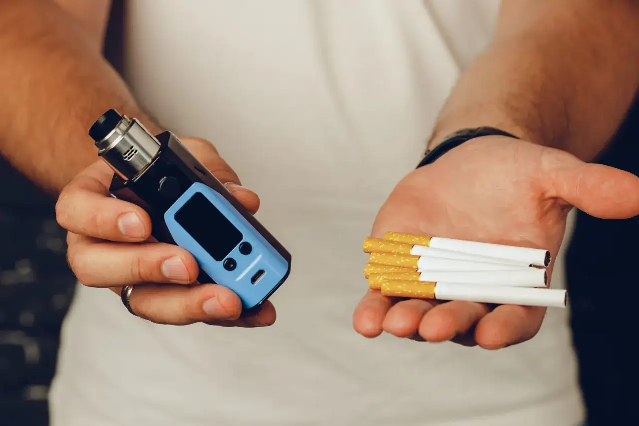 Man holds a vape in one hand and cigarettes in the other, illustrating the diferencia entre cigarrillo electronico y vaper.