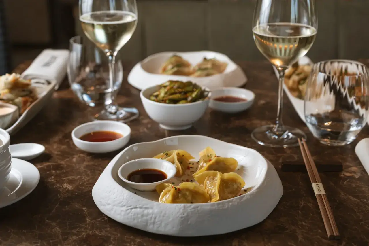Ristoranti stellati Milano: un'elegante tavola con ravioli, edamame e vino bianco, un'esperienza culinaria raffinata.