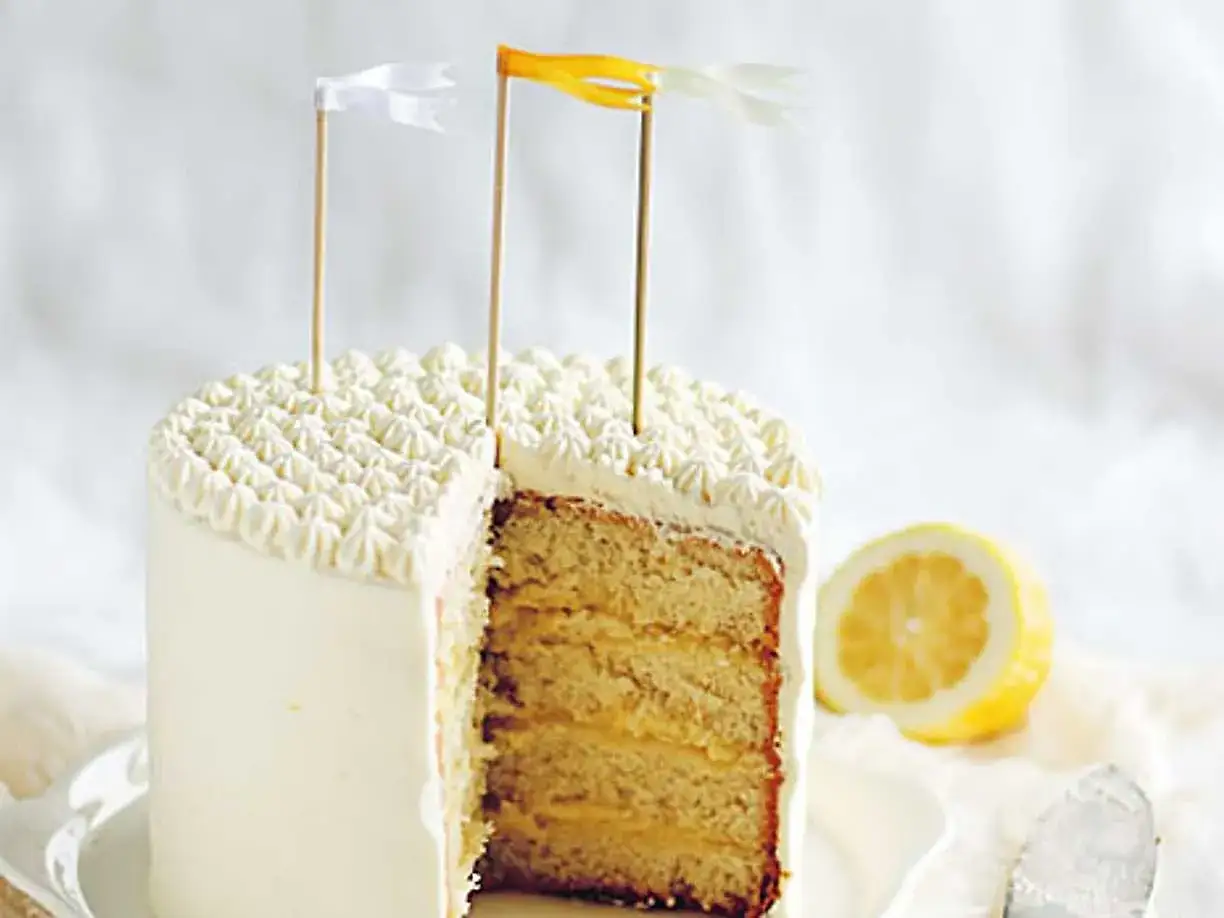 En t&aring;rta med vit frosting och dekorativa flaggor. En skiva &auml;r borttagen och visar lager av ljus botten och fyllig lemon curd.