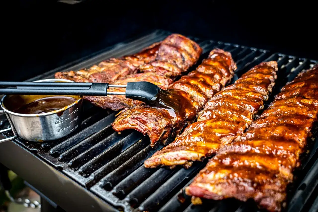 Pyszne żeberka z grilla pokryte sosem BBQ, pędzel właśnie je smaruje.