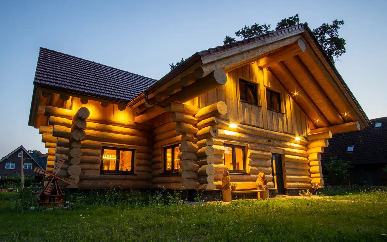 Beleuchtetes Holzhaus im Abendlicht. Ein Traum von einem Blockhaus, der die Frage nach den Holzhaus Kosten aufwirft.
