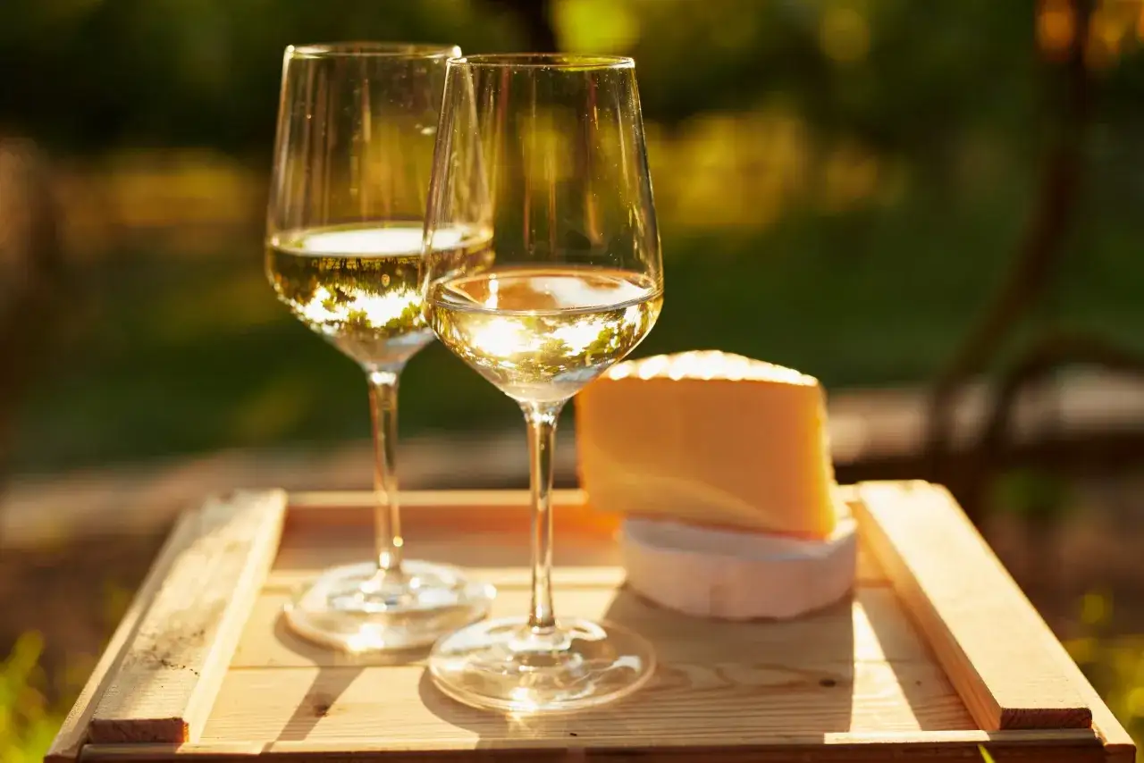 Due calici di vini aromatici dorati, con un pezzo di formaggio, su un vassoio di legno al tramonto.